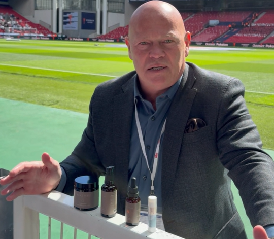 Stig Tøfting præsenterer REN LYKKE hudplejeprodukter på en fodboldbane